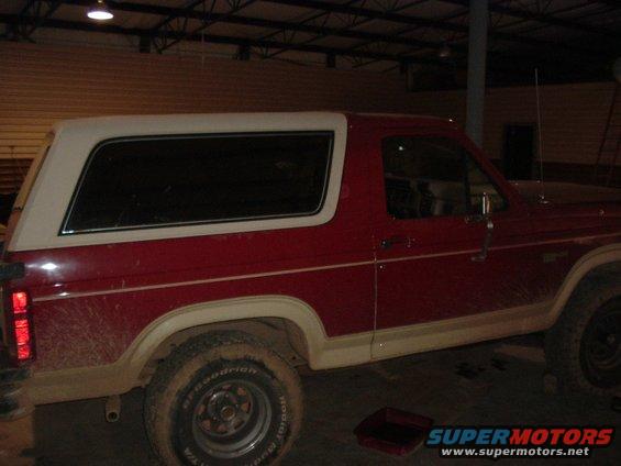 Side view of a red and white SUV, possibly a Ford Bronco from the early 1980s