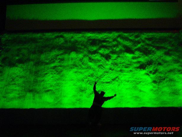 Person with arms raised against a bright green textured wall, with a dark horizontal band above