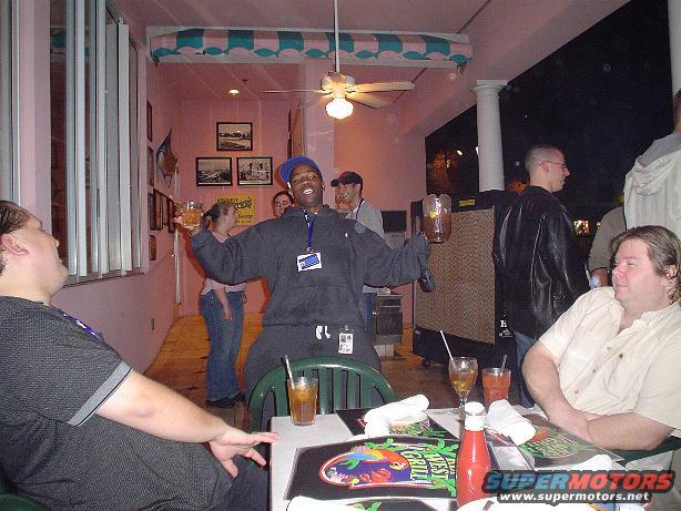 People gathered at tables inside a restaurant with pink walls and a ceiling fan