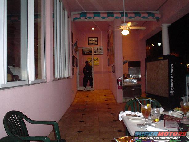 Outdoor seating area with pink walls, tables with drinks, and a person standing in a doorway