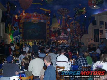 Crowded restaurant interior with a large, colorful mural depicting amusement park rides and characters on the ceiling and walls