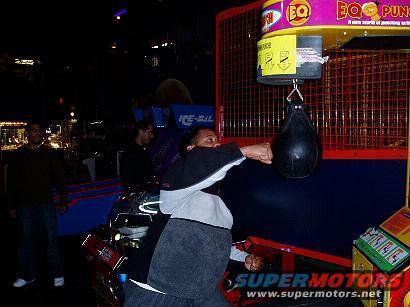Arcade game with punching bag and person punching it, with "SUPERMOTORS.NET" watermark
