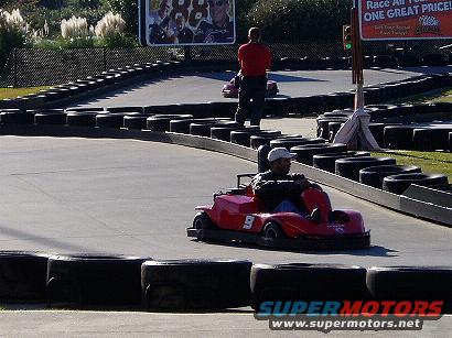Go-karts race on a track with tire barriers and a billboard in the background