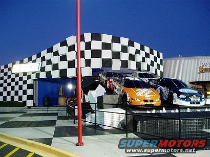 Three race cars displayed in front of a checkered building
