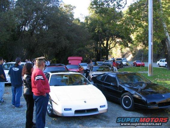 White and black Pontiac Fieros parked outside with people around