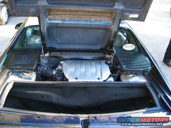 Engine bay of a dark-colored car with the hood open. Text on sticker reads 'NO DUES'
