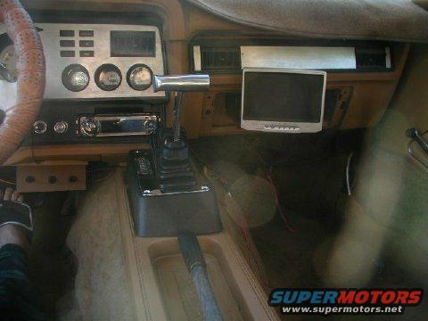 Car interior showing dashboard, steering wheel, gear shifter, and an aftermarket screen mounted on the dash