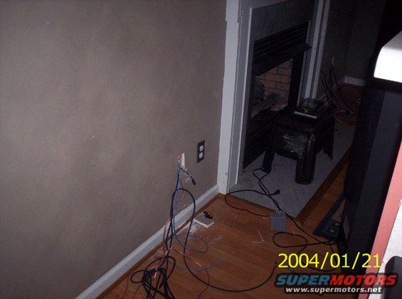 Wires are coming out of an electrical outlet and running across the floor towards a fireplace