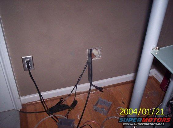 Wall with exposed electrical box, outlet, and loose wires on wooden floor
