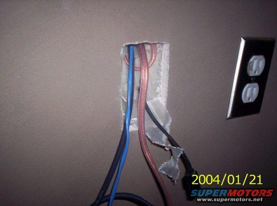 Exposed wires emerging from a wall opening next to a double electrical outlet