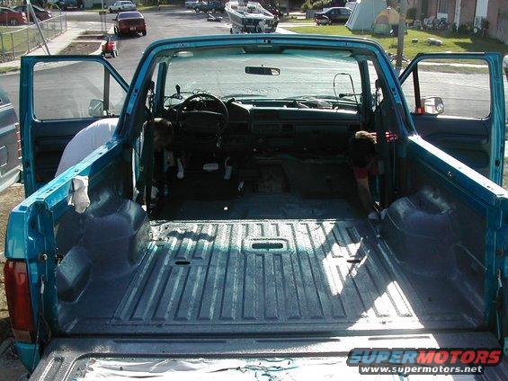 Interior and bed of a teal pickup truck with doors open. Dashboard and steering wheel visible