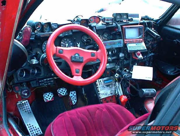 Red 1986 Pontiac Fiero interior with aftermarket steering wheel, dashboard modifications, and custom pedals