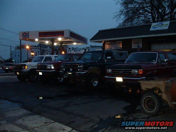 Several SUVs parked in a row at a gas station at dusk. One is a red Ford Bronco