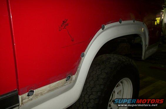 close-up of red vehicle fender with white fender flare, showing rust holes and repair marks