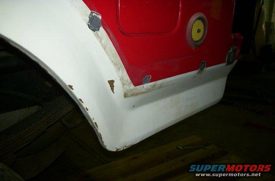 Close-up of a red and white vehicle's rear fender, showing rust spots and repair patches