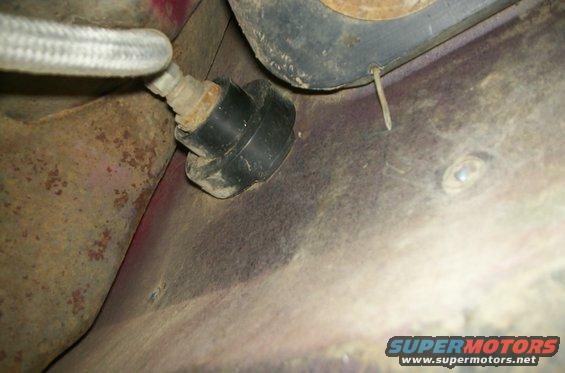Underside of vehicle showing a black rubber grommet attached to rusty metal and a braided metal hose
