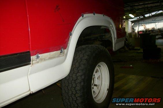 Side view of red and white Ford Bronco with fender flares being installed