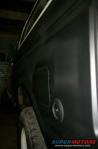 Vehicle rear quarter panel showing fuel door and gas cap. Tire visible