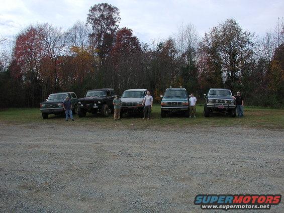 Several SUVs and trucks parked in a gravel lot with trees in the background