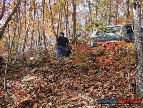 guy walking near blue off-road vehicle on wooded trail with fall leaves