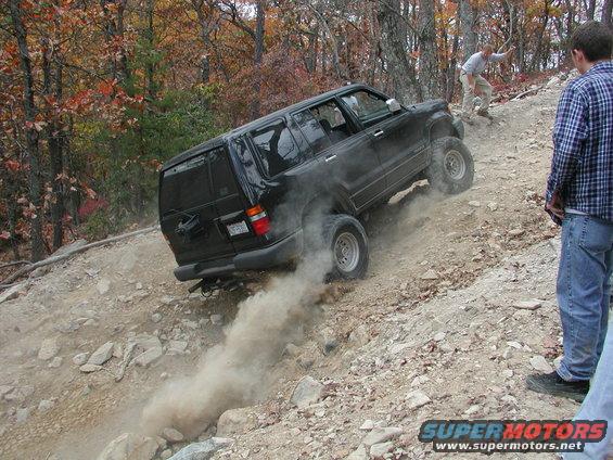 Black SUV kicking up dust while climbing a steep, rocky trail with two people watching