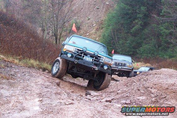 Green Ford Bronco and other off-road vehicles navigating a steep, muddy incline. License plate visible