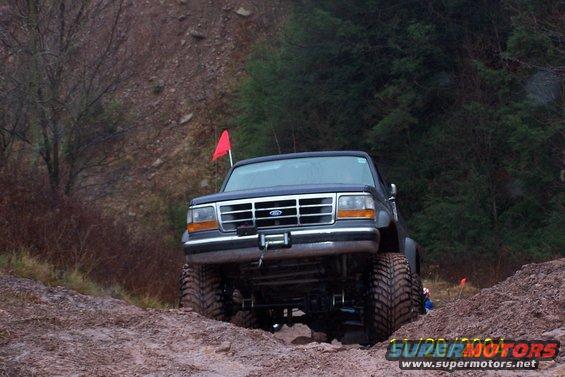 Ford F-Series truck with large tires driving on a dirt trail
