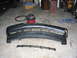 1995 Ford Taurus - A detached front bumper and grille assembly lies on a concrete floor, with a shop vacuum and other items in the background.
