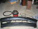 1995 Ford Taurus - A detached car bumper lies on a garage floor next to a shop vacuum and various cords.