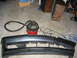 1995 Ford Taurus - A detached car bumper lies on a concrete floor next to a shop vacuum and various cords.
