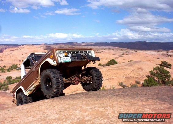 Brown 1974 Ford Bronco climbing a rock formation, front-left tire elevated