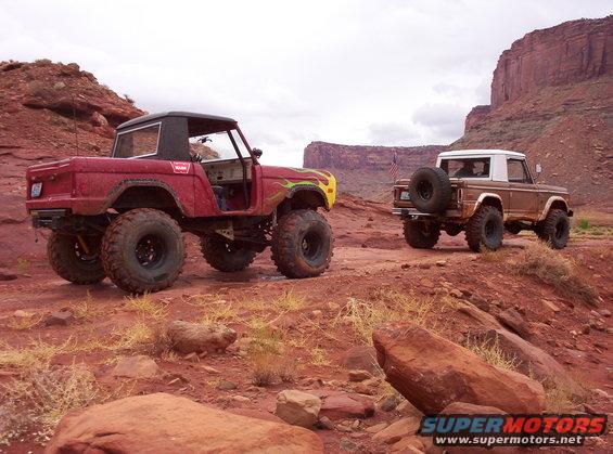 Red 1974 Ford Bronco with flame decals and lifted suspension, parked next to a brown 1974 Ford Bronco with a spare tire on the back