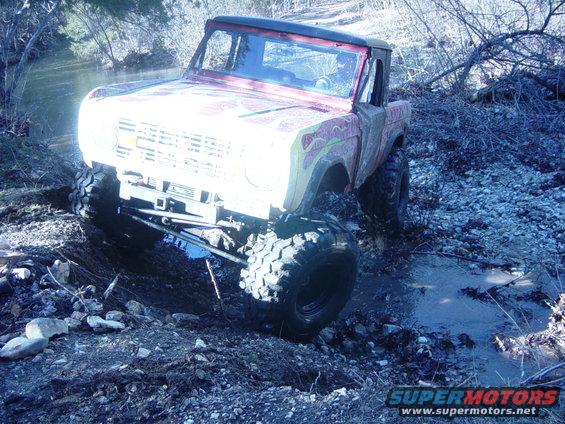 Red Ford Bronco with flame decals driving through mud and water