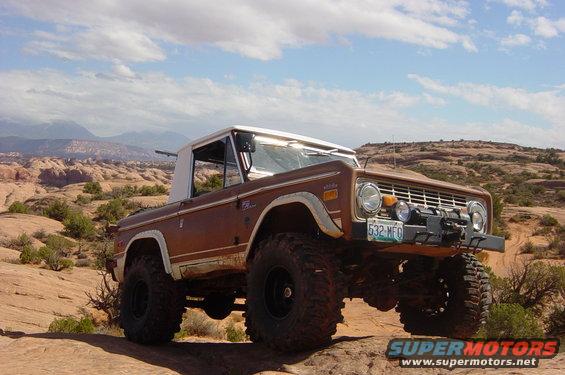Brown 1974 Ford Bronco with white top and large tires on rocky terrain
