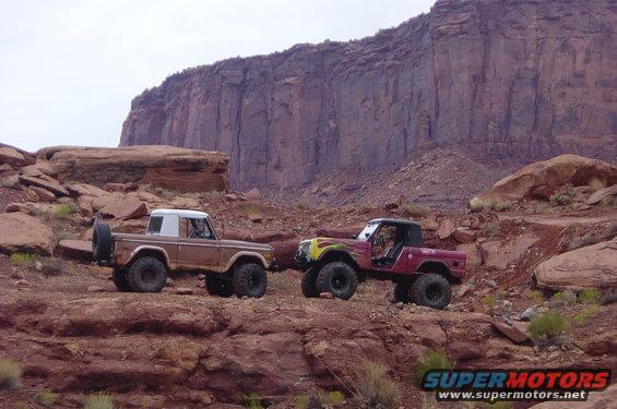 Two 1974 Ford Broncos parked on rocky terrain with a large cliff face in the background