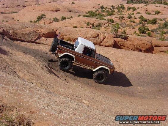 Brown 1974 Ford Bronco with white top and spare tire on rear, climbing a rocky incline