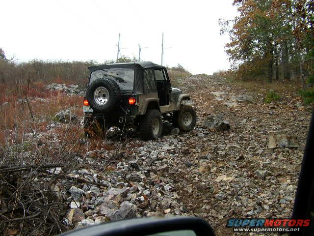 Jeep Wrangler driving up a rocky hill, spare tire mounted on the back