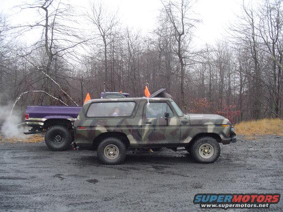 Camouflaged SUV parked next to a purple pickup truck emitting smoke
