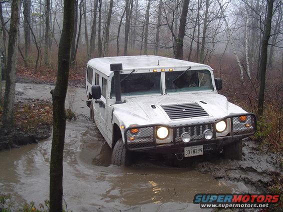 White Hummer H1 driving through mud and water in a forest