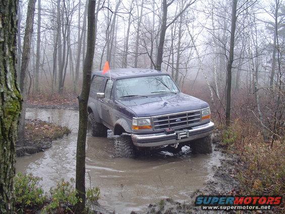 Blue Ford Bronco driving through a muddy trail in a forest
