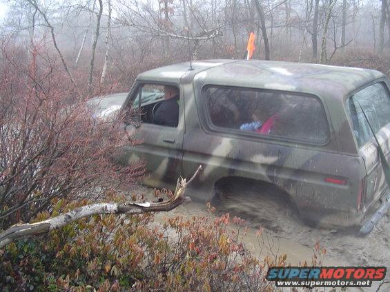 Camouflaged 1978 Ford Bronco stuck in mud, side view