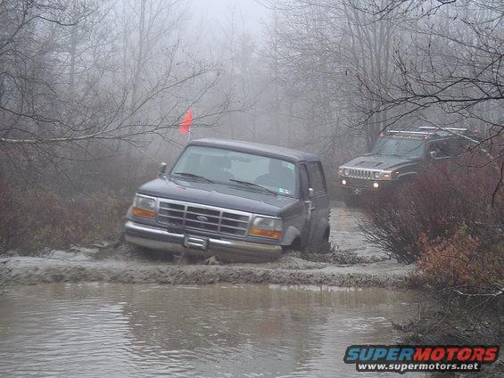 Dark blue SUV stuck in mud, 1995 model year suggested by body style. Another SUV is visible behind it