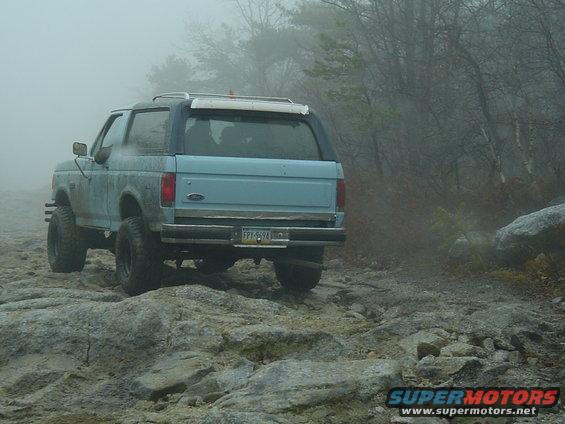 Light blue SUV with a dark blue roof, lifted suspension, and off-road tires, driving on a rocky, foggy trail