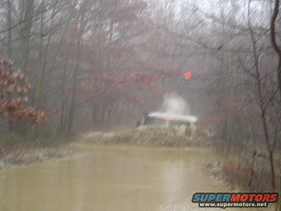 White SUV driving through a muddy water obstacle course in a wooded area