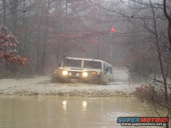 Hummer H1 driving through mud and water in a wooded area