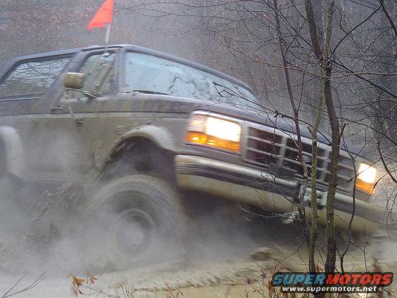 1993 Ford Bronco driving through mud with orange flag on roof