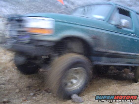 Green SUV with a damaged front bumper and off-road tires on a dirt path