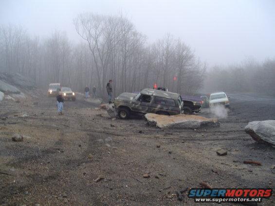 Camouflaged SUV stuck on rocks with other vehicles in background