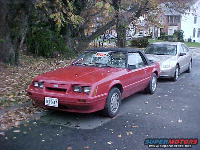 Red convertible Mustang parked on street next to a silver sedan. License plate reads 1X0-3617