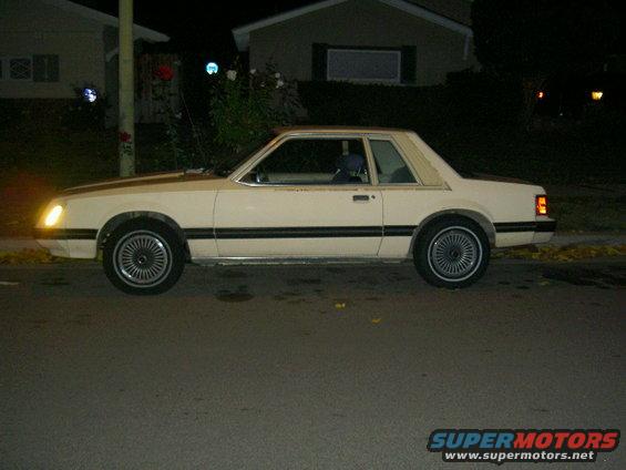 Side view of a white 1982 Ford Mustang parked on a street at night